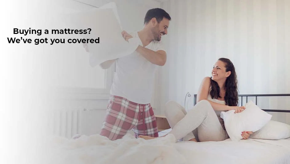 Happy couple having a playful pillow fight on a comfortable white bed.