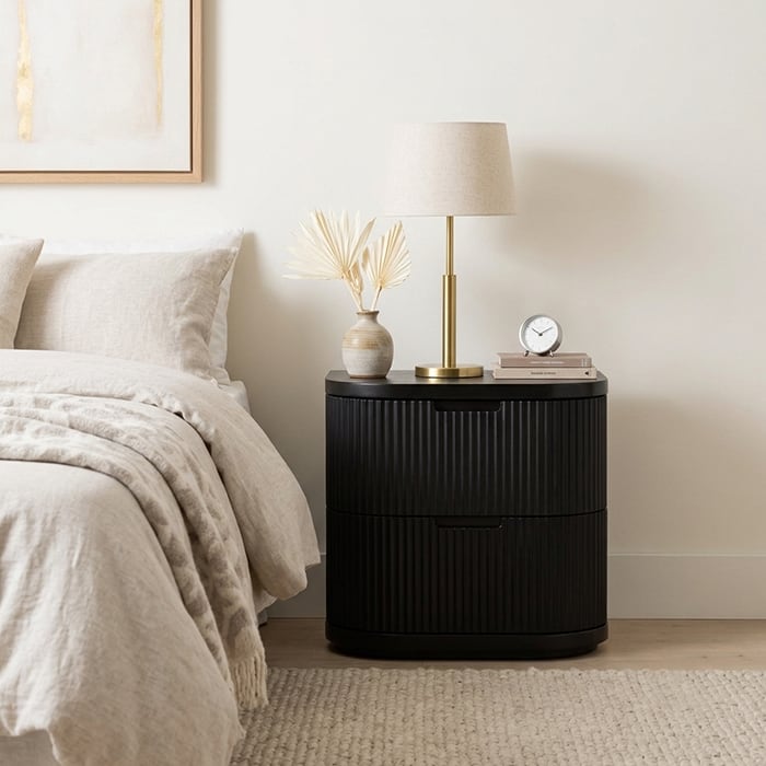 Black fluted bedside table with a lamp and clock